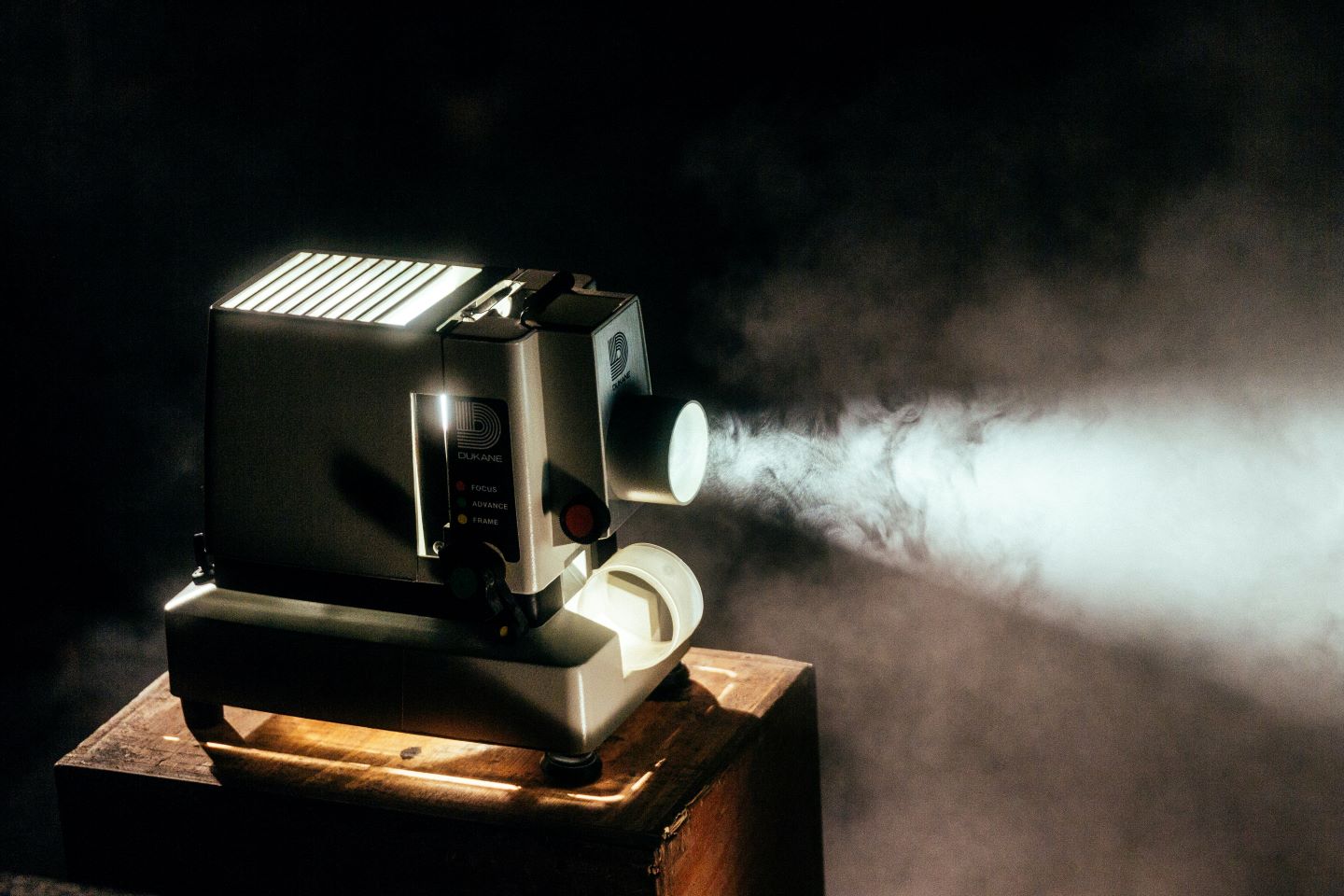 Old school film projector with light projecting from lens into smoky room