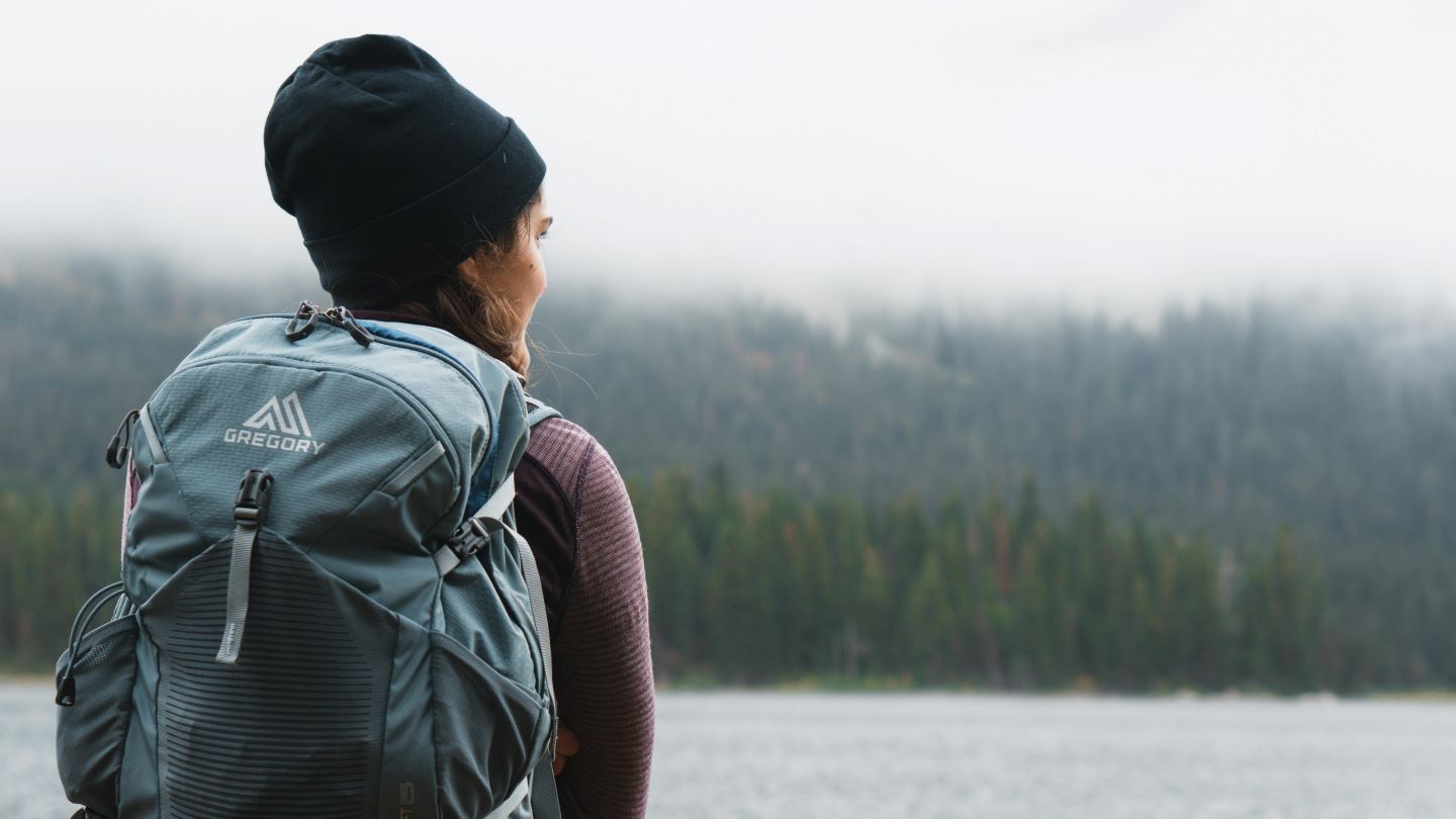 Woman in black beenie with hiking bag on looking out over a lakefront